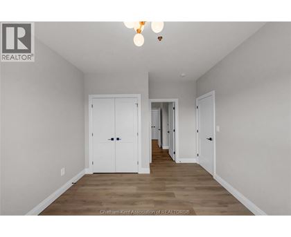 A spacious room with white walls and wooden flooring, featuring a row of white doors.