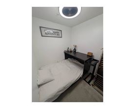 A small bedroom with a bed, a desk, and a sign on the wall that says "Adventure".