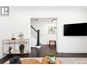 A living room with a black sofa and a TV on the wall.