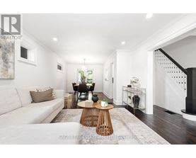 A well-lit, spacious living room with a white sofa, wooden coffee table, and a staircase on the right.