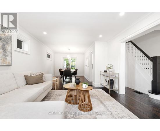 A well-lit, spacious living room with a white sofa, wooden coffee table, and a staircase on the right.