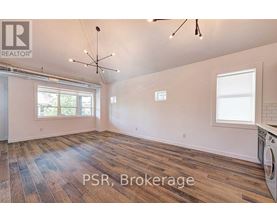 A large, empty room with wood flooring and a washing machine in the corner.