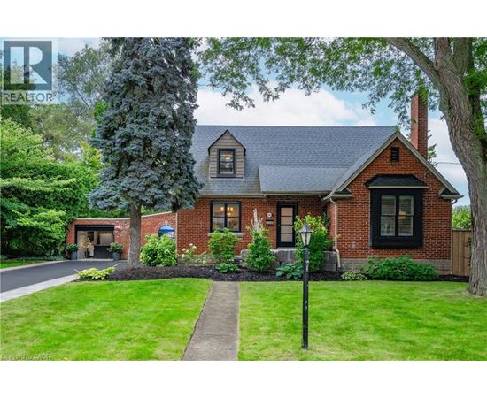 A house with a red brick exterior and a black roof is surrounded by greenery.