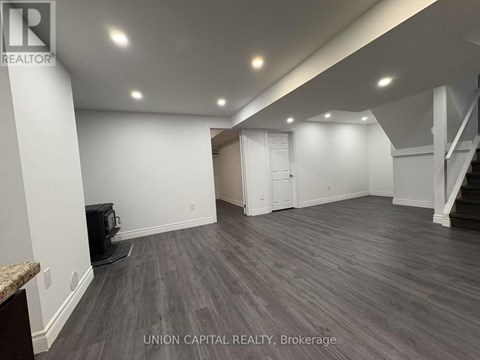 A spacious room with wood flooring and white walls, with a staircase on the right side.