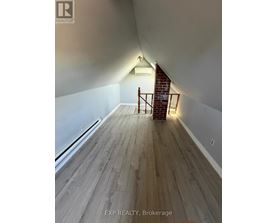 A room with wooden floors and a staircase leading to a brick wall.