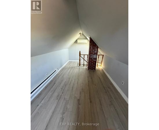A room with wooden floors and a staircase leading to a brick wall.