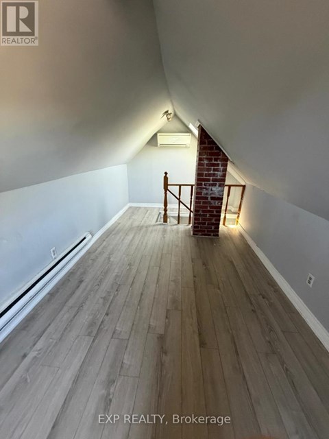 A room with wooden floors and a staircase leading to a brick wall.