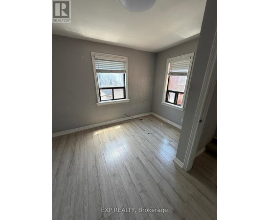 A room with wooden flooring and two windows.