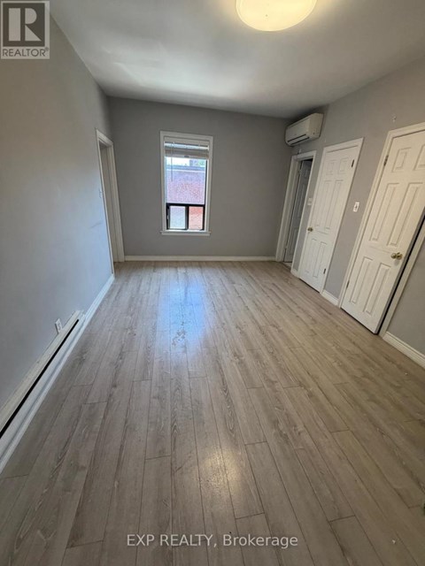 A room with wooden flooring and a window with a view of a red building outside.