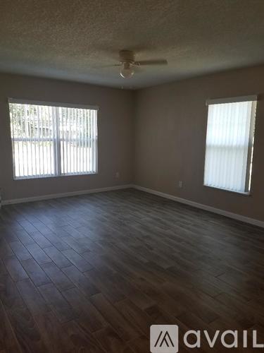 A room with wooden flooring and two windows.