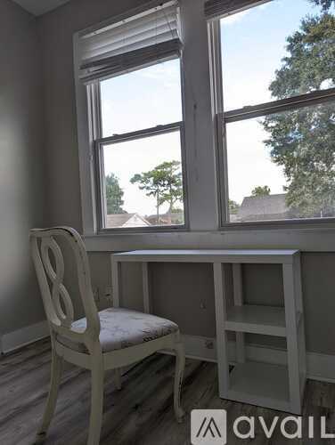 A white chair is in front of a window with a view of trees and houses.