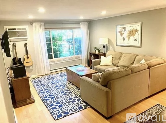 A living room with a couch, a guitar, a speaker, and a window.