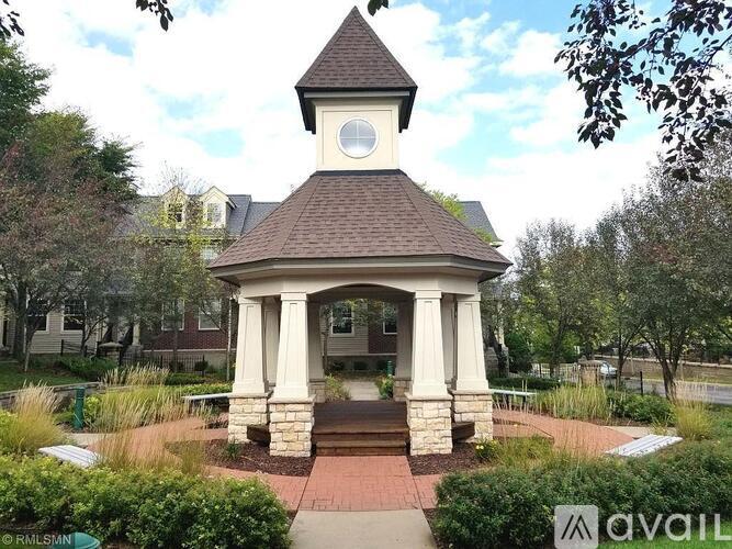 A gazebo with a brown roof and a white clock is surrounded by greenery.