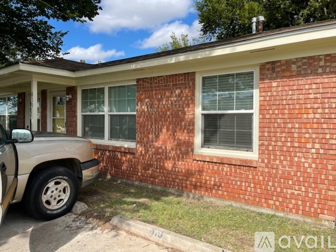 A beige car is parked in front of a red brick house.