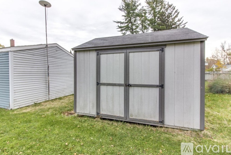 A grey shed with a black roof is situated in a grassy area.