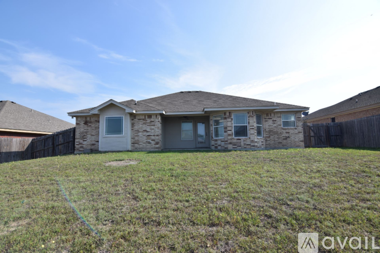 A house with a stone facade and a brown roof is surrounded by a grassy area.