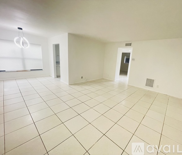 A spacious room with white tiled flooring and a doorway leading to another room.