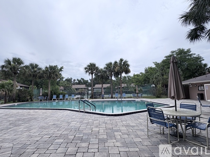 A pool surrounded by palm trees and a patio area with chairs and an umbrella.