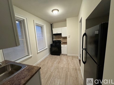 A kitchen with a black fridge, brown countertop, and a window with blinds.