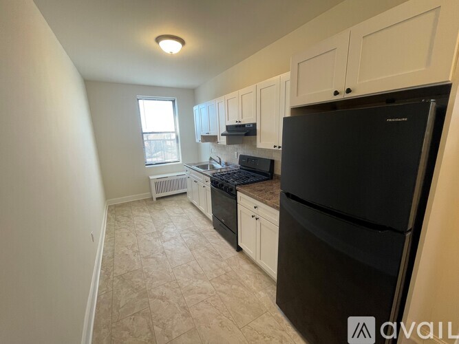 A kitchen with a black fridge, white cabinets, and a window.
