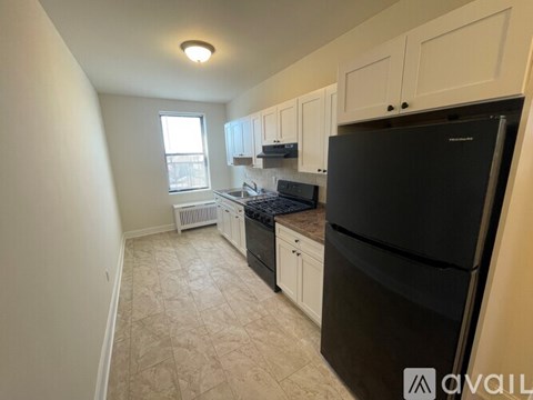 A kitchen with a black fridge, white cabinets, and a window.