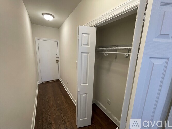 A hallway with a white door and a white closet with shelves.