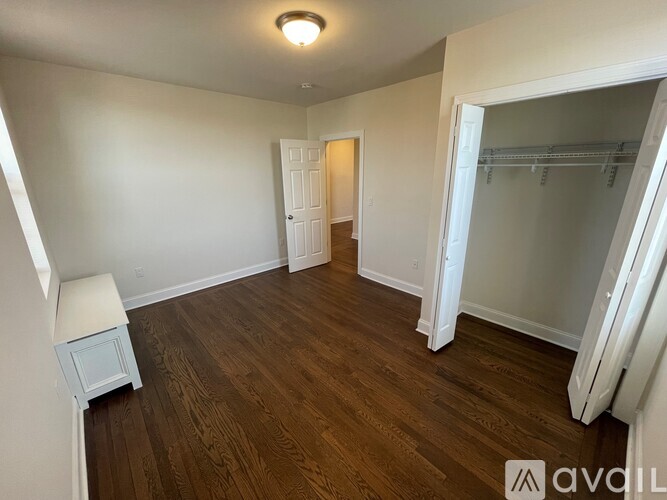 A room with wood flooring and white walls, with a small white cabinet and a closet with a white door.