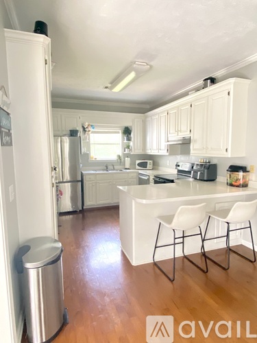 A kitchen with white cabinets and a white island with two chairs.