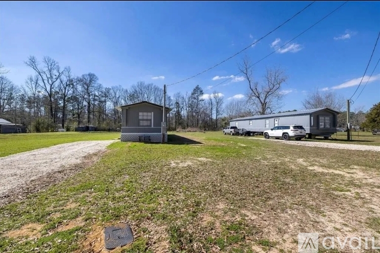 A house and a trailer are parked in a grassy area with trees in the background.