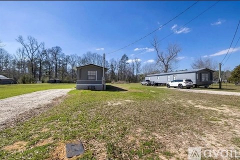 A house and a trailer are parked in a grassy area with trees in the background.