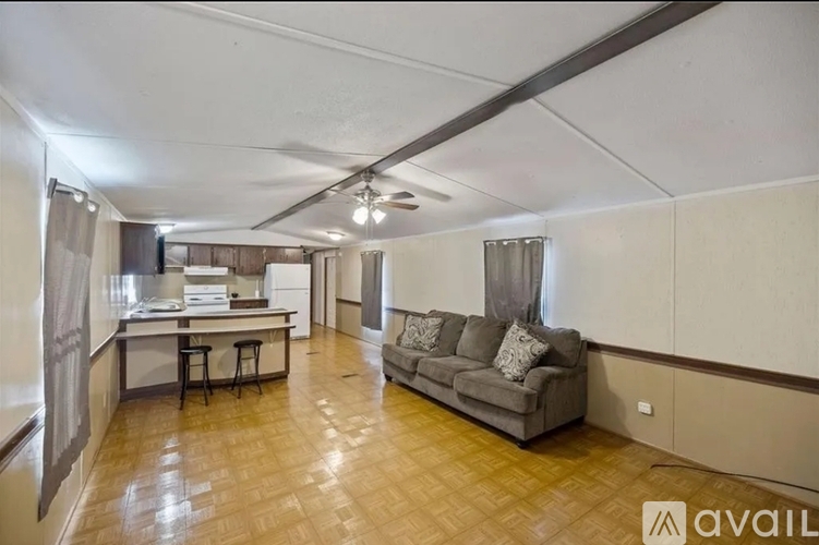 A spacious living room with a grey sofa and a kitchen area in the background.