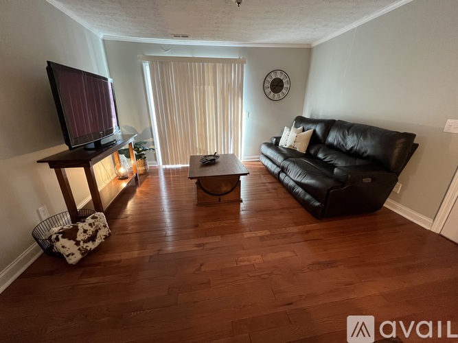A living room with a black leather couch and a wooden floor.