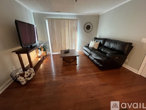 A living room with a black leather couch and a wooden floor.