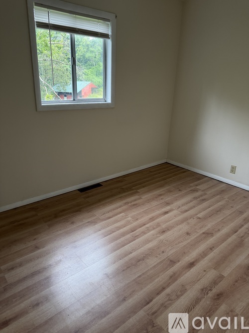 A room with wooden flooring and a window showing a view of a red building outside.