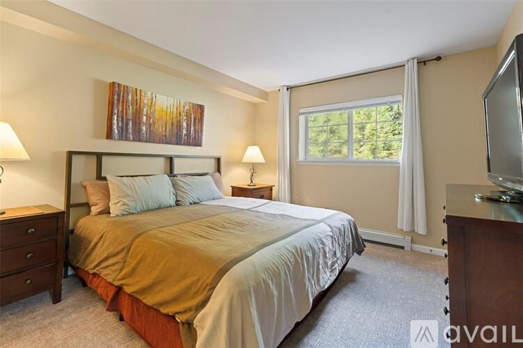 A bedroom with a large bed, a painting on the wall, and a window with curtains.
