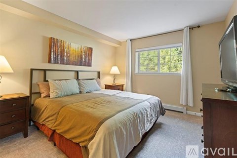 A bedroom with a large bed, a painting on the wall, and a window with curtains.
