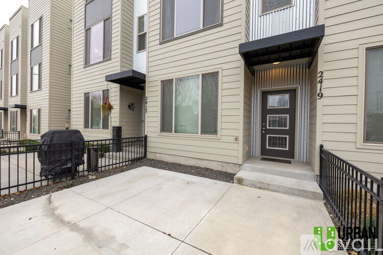 A black grill is on the patio of a beige townhouse.