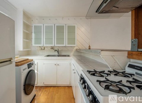 A kitchen with a white stove top oven and white cabinets.