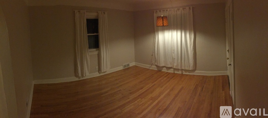 A room with wooden floors and two windows with curtains.