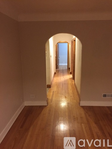 A hallway with wooden floors and white walls leading to a door at the end.