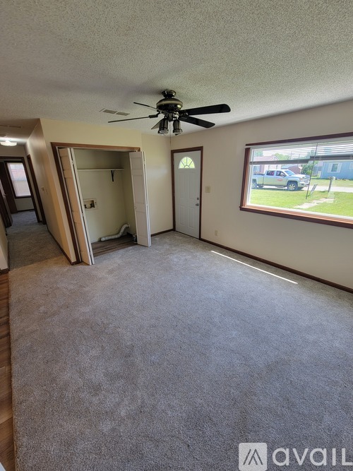 A room with a ceiling fan and a window overlooking a parking lot.