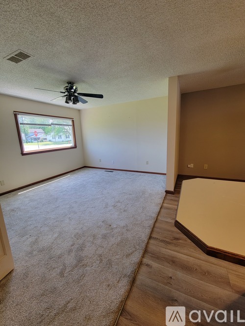A room with a carpeted floor, a ceiling fan, and a window.