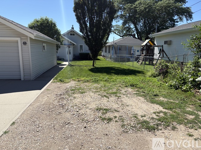 A gravel area in front of a house with a tree and a fence.