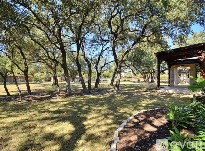 A gazebo sits in the middle of a grassy area with trees surrounding it.