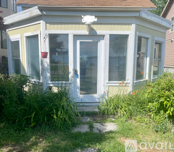 A small white house with a yellow stripe and a red flower hanging from the window.