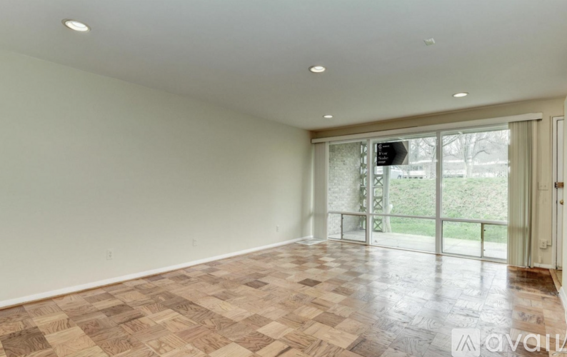 A spacious room with a wooden floor and sliding glass doors leading to a balcony.