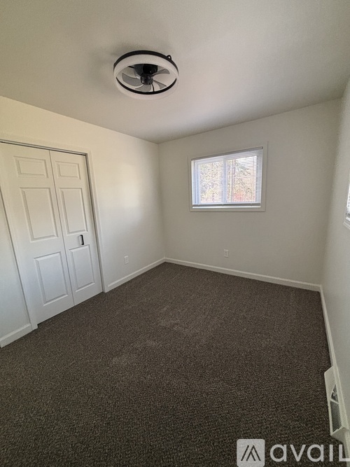 A room with a carpeted floor, a ceiling fan, and a window with blinds.