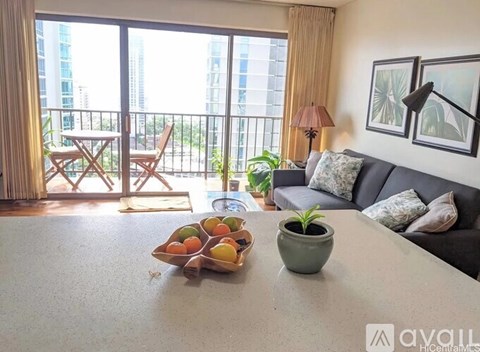 A living room with a grey couch, a table with a bowl of fruit and a potted plant.