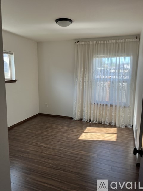 A room with wooden flooring and a window with white curtains.
