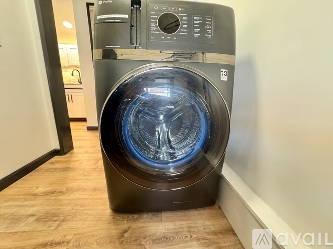 A front load washing machine with a transparent door is placed in a room.